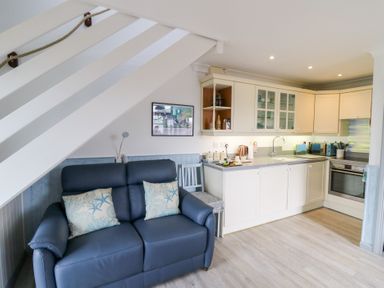 A kitchen with white cabinets and a blue sofa with cushions under a staircase at 5 The Coach House in Broad haven Pembrokeshire