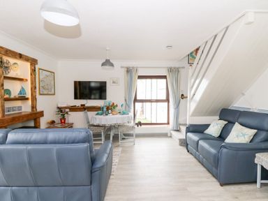 A living room with blue sofas a dining table under a window and a wall-mounted TV at 5 The Coach House in Broad haven Pembrokeshire
