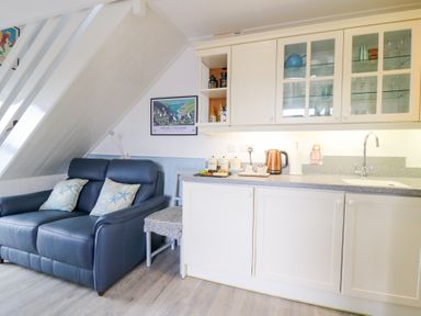 A small kitchen area with cream cabinets and a blue sofa with cushions at 5 The Coach House in Broad haven Pembrokeshire