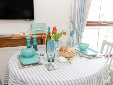A dining table set with blue tableware and tulips in a room with a window and curtain at 5 The Coach House Broad haven Pembrokeshire