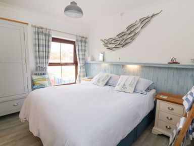 A bedroom with a bed pillows bedside tables and a window with checked curtains at 5 The Coach House in Broad haven Pembrokeshire