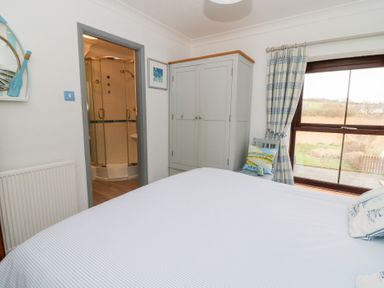 A bedroom with a bed a wardrobe a chair with cushions a window and an ensuite bathroom at 5 The Coach House in Broad haven Pembrokeshire