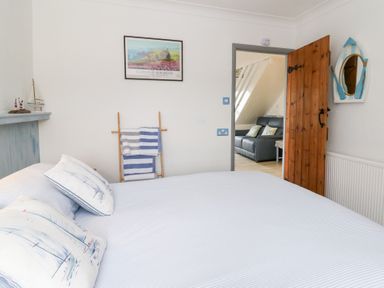 A bedroom with a bed and pillows with boat images and an open wooden door showing a living room with a sofa at 5 The Coach House Broad haven Pembrokeshire