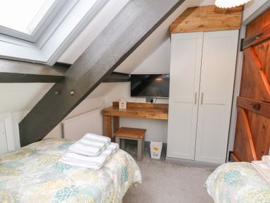 A bedroom with two beds towels on them a wooden desk and stool a wall mounted tv and a wardrobe at 5 The Coach House Broad haven Pembrokeshire