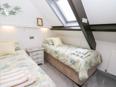 A bedroom with two single beds a small bedside table and a skylight window at 5 The Coach House in Broad haven Pembrokeshire