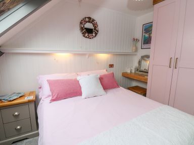 A bedroom with a bed pink pillows a bedside table and a wardrobe at 5 The Coach House in Broad haven Pembrokeshire