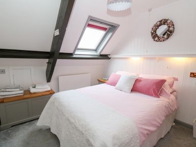 A bedroom with a bed pink pillows and window at 5 The Coach House in Broad haven Pembrokeshire