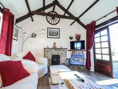 A living room with white sofas and red cushions a stone fireplace a television tourist information leaflets and red curtains at Y Stabl in Fishguard Pembrokeshire