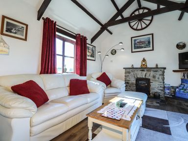 A living room with white sofas red cushions a stone fireplace and a wooden coffee table at Y Stabl in Fishguard Pembrokeshire