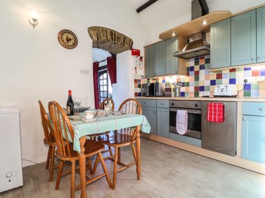 A kitchen with a dining table and four wooden chairs and blue cabinets at Y Stabl Fishguard Pembrokeshire