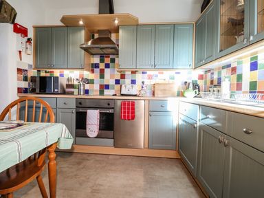 A kitchen with green cabinets colorful tiled backsplash a microwave oven and a wooden chair at Y Stabl Fishguard Pembrokeshire