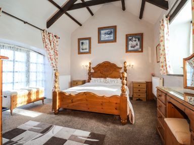 A bedroom with a wooden bed wooden furniture and floral curtains at Y Stabl in Fishguard Pembrokeshire