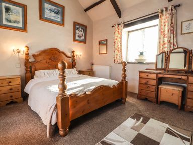 A bedroom with a wooden bed dresser and nightstands and floral curtains at Y Stabl in Fishguard Pembrokeshire