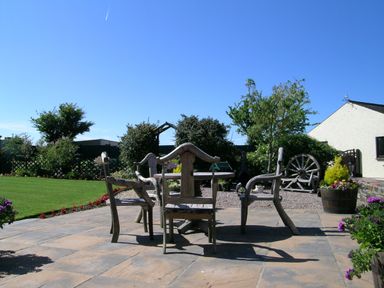 An outdoor patio with wooden chairs and table surrounded by plants and a lawn at Y Stabl in Fishguard Pembrokeshire