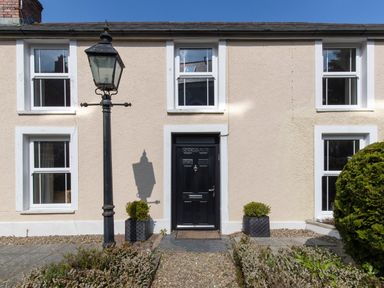 The front of a beige house with a black door two symmetrical windows and a black street lamp at The Rock House in Fishguard Pembrokeshire