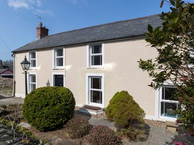 The exterior of a two-story house with multiple windows a black front door shrubs and a stone pathway at The Rock House in Fishguard Pembrokeshire