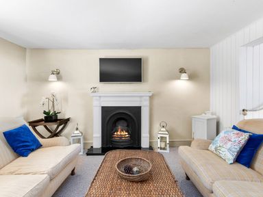A living room with a fireplace two sofas a woven coffee table and a TV above the fireplace at The Rock House in Fishguard Pembrokeshire