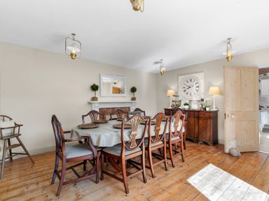 A dining room with a wooden table and chairs a cabinet with lamps and clock on wall at The Rock House in Fishguard Pembrokeshire