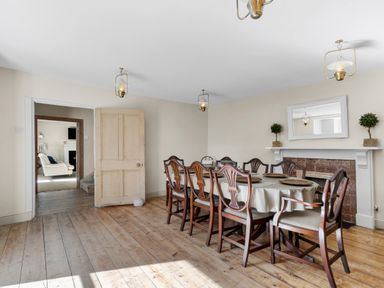 A dining room with a long table surrounded by eight chairs and a fireplace with a mirror above at The Rock House in Fishguard Pembrokeshire