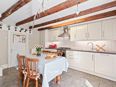 A kitchen with wooden chairs around a table covered with a tablecloth and flowers on the table at The Rock House in Fishguard Pembrokeshire
