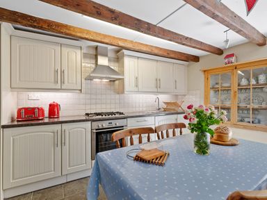 A kitchen with wooden beams white cabinets and a table with flowers and bread at The Rock House in Fishguard Pembrokeshire