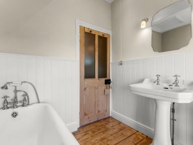 A bathroom with a bathtub sink mirror wooden door and wood floor at The Rock House in Fishguard Pembrokeshire