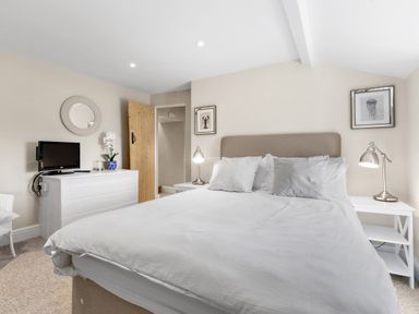 A bedroom with a bed a white dresser with a TV and flowers a wooden door and two bedside tables with lamps at The Rock House in Fishguard Pembrokeshire