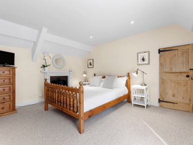 A bedroom with a wooden bed white bedding two white bedside tables lamps wooden chest of drawers and a wooden door at The Rock House in Fishguard Pembrokeshire