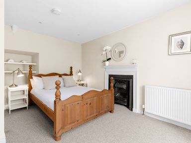 A bedroom with a wooden bed white bedside tables lamps and a fireplace at The Rock House in Fishguard Pembrokeshire