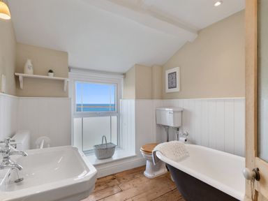 A bathroom with a sink toilet and bathtub with a window showing a sea view at The Rock House in Fishguard Pembrokeshire