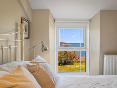 A bedroom with a bed and pillows next to a window showing a sea view at The Rock House in Fishguard Pembrokeshire