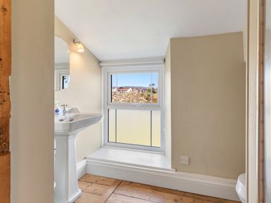 A bathroom with a pedestal sink a window with a view and wooden flooring at The Rock House in Fishguard Pembrokeshire