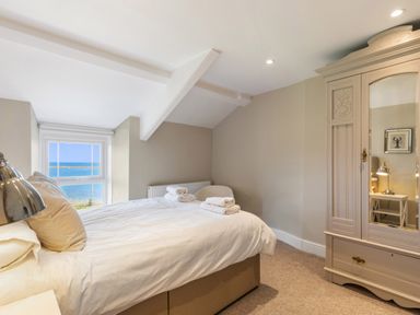 A bedroom with a bed a wardrobe a chair and a window showing the sea at The Rock House in Fishguard Pembrokeshire