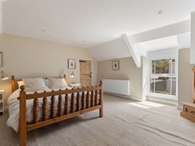 A bedroom with a wooden bed frame two bedside tables with lamps a wooden door a window and a radiator at The Rock House in Fishguard Pembrokeshire