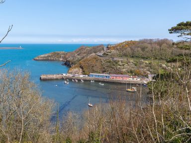 A coastal harbor with boats docked near colorful buildings and hills in the background at The Rock House in Fishguard Pembrokeshire
