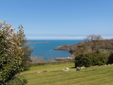 A coastal view with grass and bushes overlooking a harbor and sea at The Rock House in Fishguard Pembrokeshire