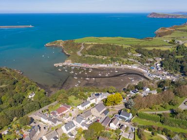An aerial view of a coastal village with boats in the harbor and green fields at The Rock House in Fishguard Pembrokeshire