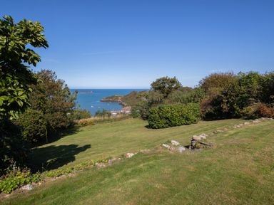 A garden with grass and bushes overlooking the sea at The Rock House in Fishguard Pembrokeshire