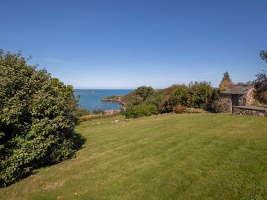 A grassy garden with bushes a stone shed and a view of the sea at The Rock House in Fishguard Pembrokeshire