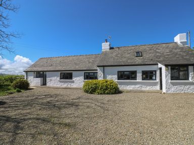A white cottage with a stone roof and gravel driveway surrounded by bushes at Ty-Newydd Cottage in Nevern near Newport Pembrokeshire