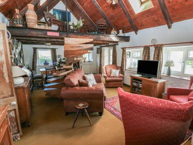 A living room with brown sofas a red armchair wooden furniture and spiral staircase at Ty-Newydd Cottage in Nevern near Newport Pembrokeshire