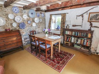 A dining room with a wooden table and chairs on a rug with decorative plates on a stone wall at Ty-Newydd Cottage in Nevern near Newport Pembrokeshire