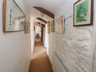 A narrow hallway with framed pictures on the walls and wooden beams on the ceiling at Ty-Newydd Cottage in Nevern near Newport Pembrokeshire