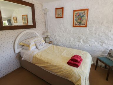 A single bed with yellow check bedding and folded red towels in a small bedroom with framed pictures and a chair at Ty-Newydd Cottage in Nevern near Newport Pembrokeshire