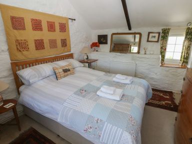 A bedroom with a double bed bedside tables a wall mirror and a window at Ty-Newydd Cottage in Nevern near Newport Pembrokeshire