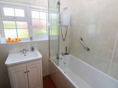 A bathroom with a bathtub and shower a sink with cabinet and a window with rubber ducks on the sill at Ty-Newydd Cottage in Nevern near Newport Pembrokeshire