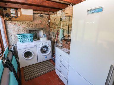 A laundry room with a washing machine, dryer, white fridge, wicker basket, and cleaning tools at Ty-Newydd Cottage in Nevern near Newport Pembrokeshire