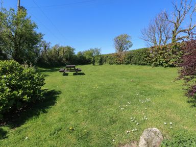 A grassy garden area with a wooden picnic table surrounded by bushes and trees at Ty-Newydd Cottage in Nevern near Newport Pembrokeshire