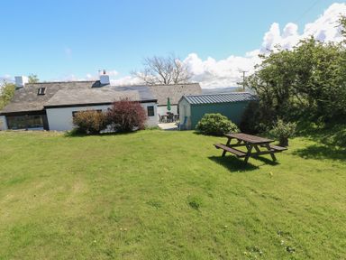 A grassy garden with a picnic table a small shed and a house with bushes at Ty-Newydd Cottage in Nevern near Newport Pembrokeshire
