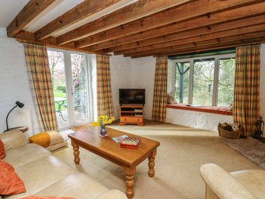 A living room with wooden beams a coffee table with flowers a television and a window seat at Trawsnant Cottage in New Quay Ceredigion